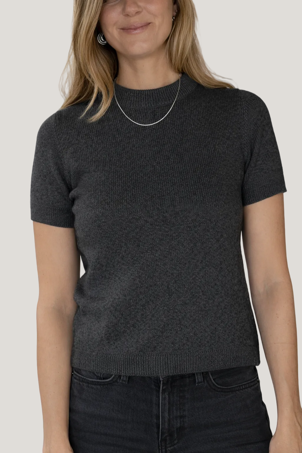Woman wearing a dark gray short-sleeve knit top against a white background