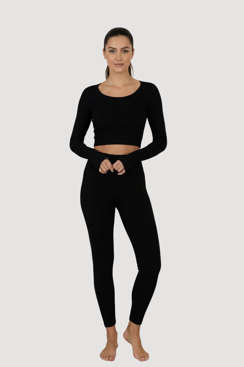 A woman modeling a black long-sleeve crop top and matching black leggings against a light gray studio background.