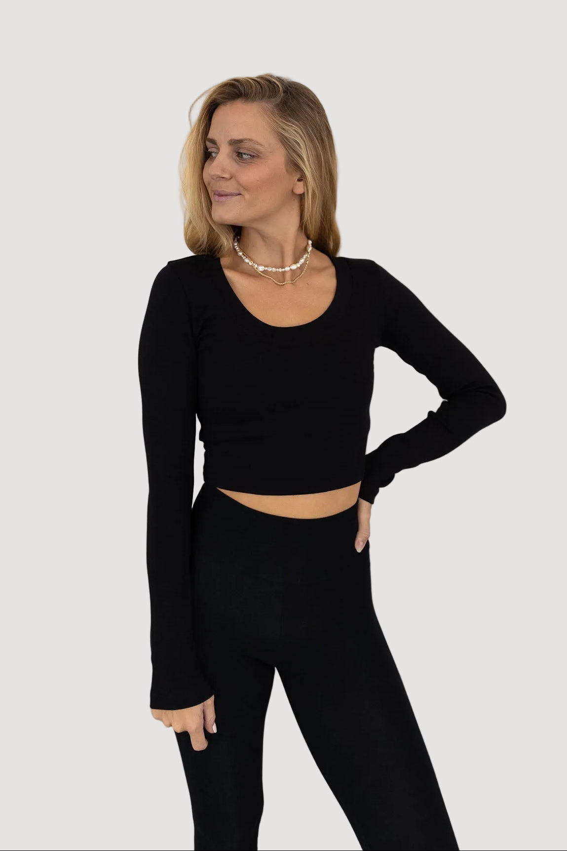 A person wearing a black longsleeve crop top with a rounded neckline, standing against a white background.