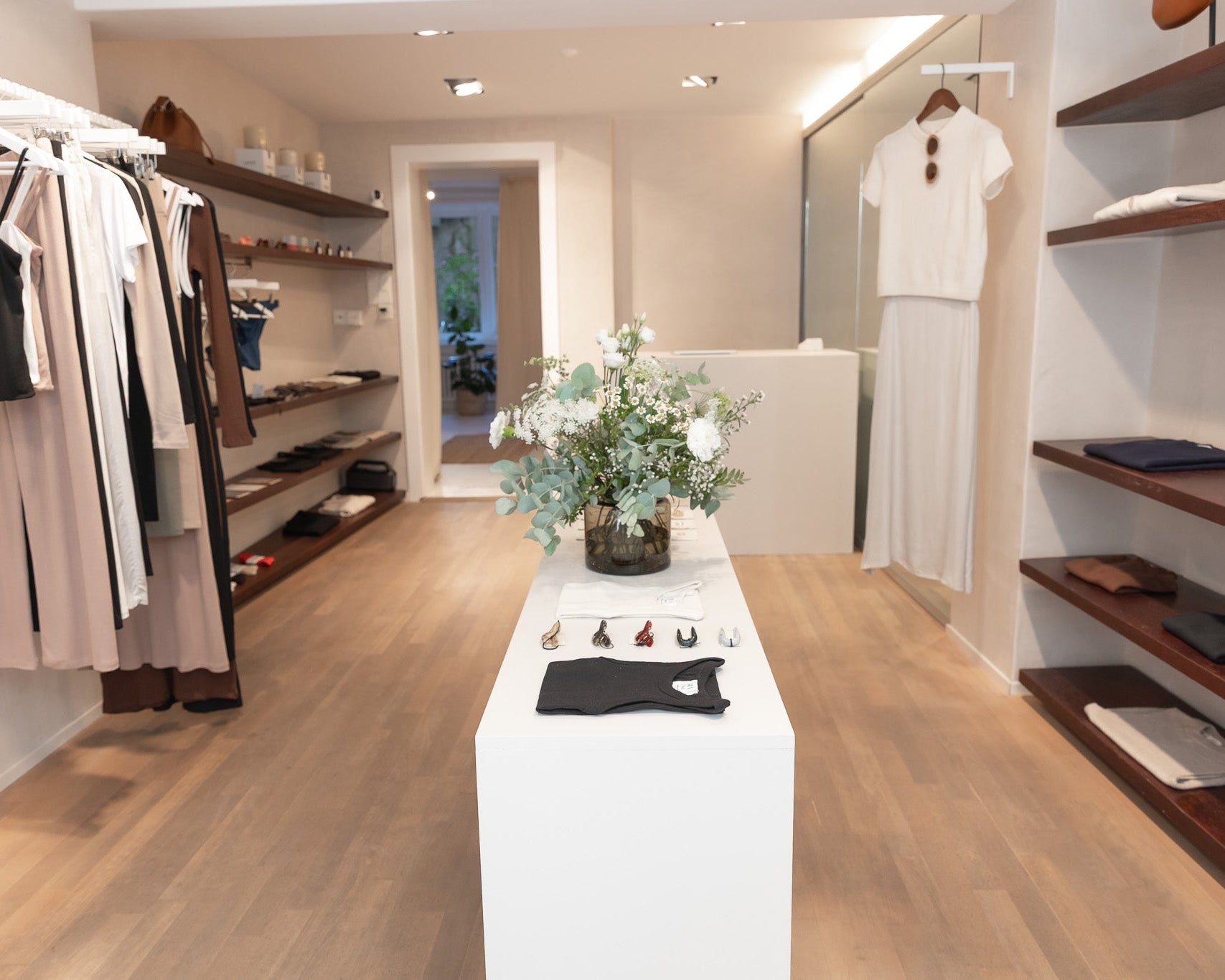 A boutique interior with clothing racks, shelving, and a central white pedestal displaying a floral arrangement and small accessories. No person is present, but the real retail environment makes this Lifestyle rather than Product/Packaging.