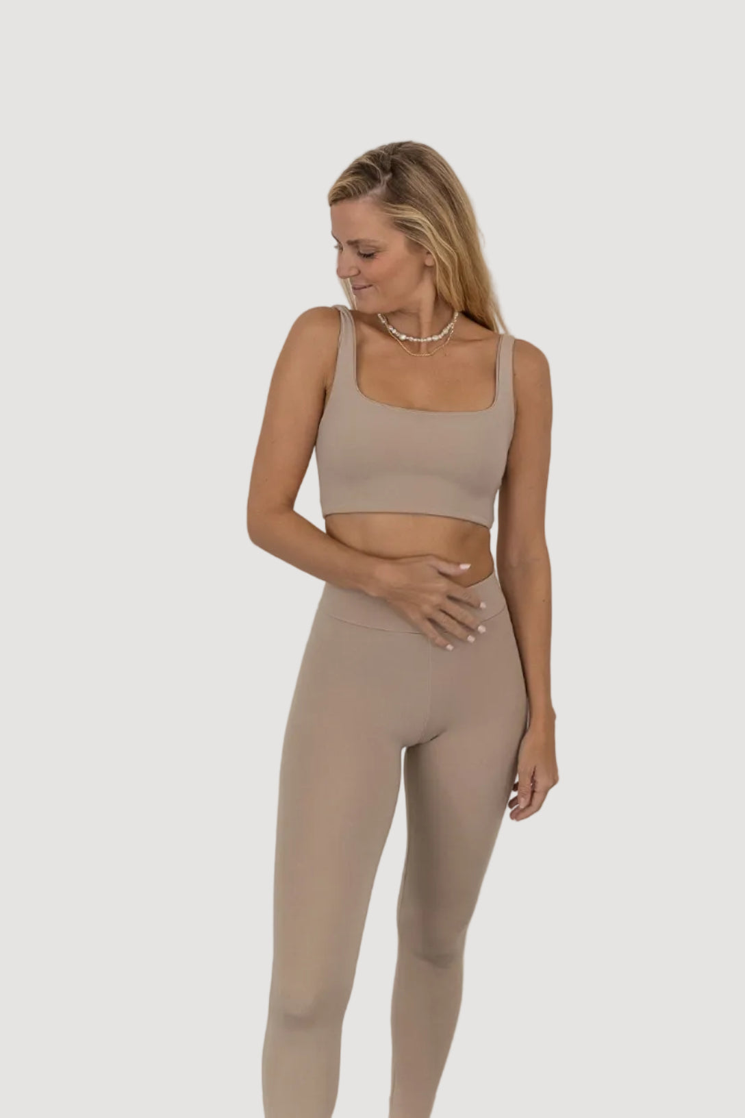 A female model wearing a beige sleeveless top and matching leggings made from Tencel fabric, standing against a plain background.