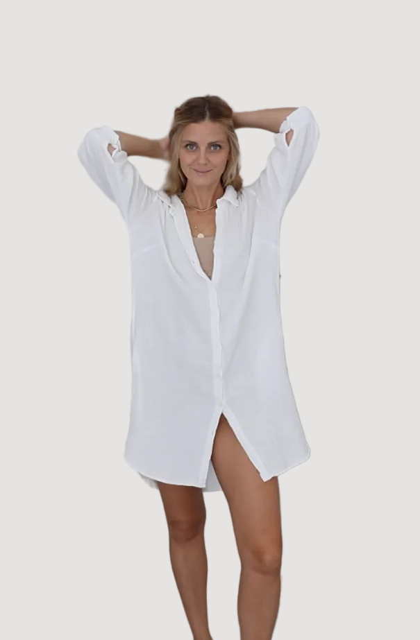 A model wearing a white high-quality fabric shirtdress with pockets, standing against a grey background.