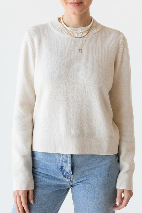 Woman wearing a cream sweater and light blue jeans on a white background