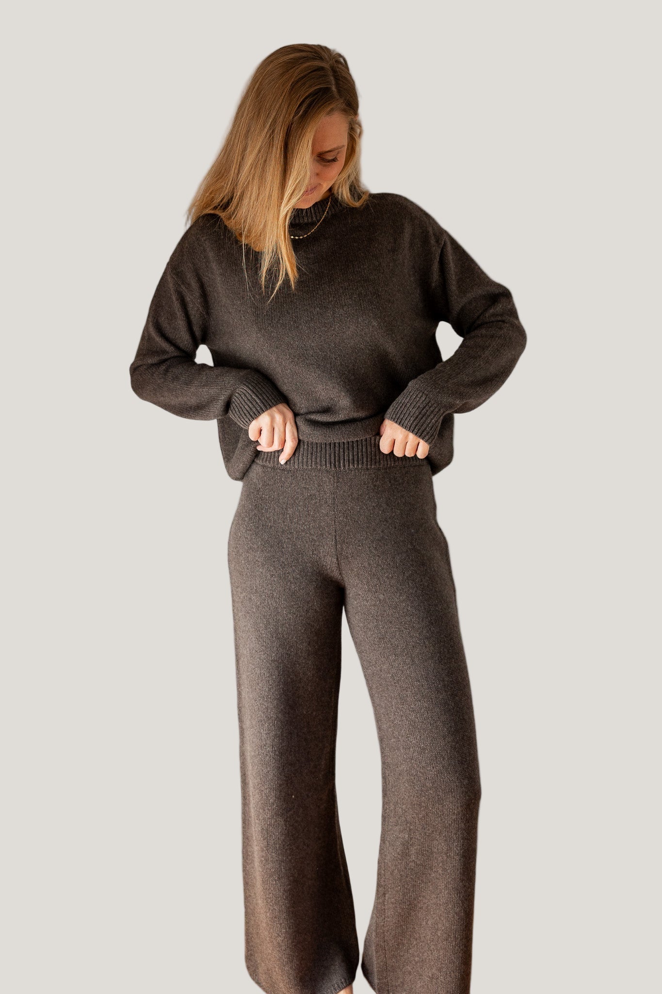 Woman wearing a dark gray sweater and pants on a light background
