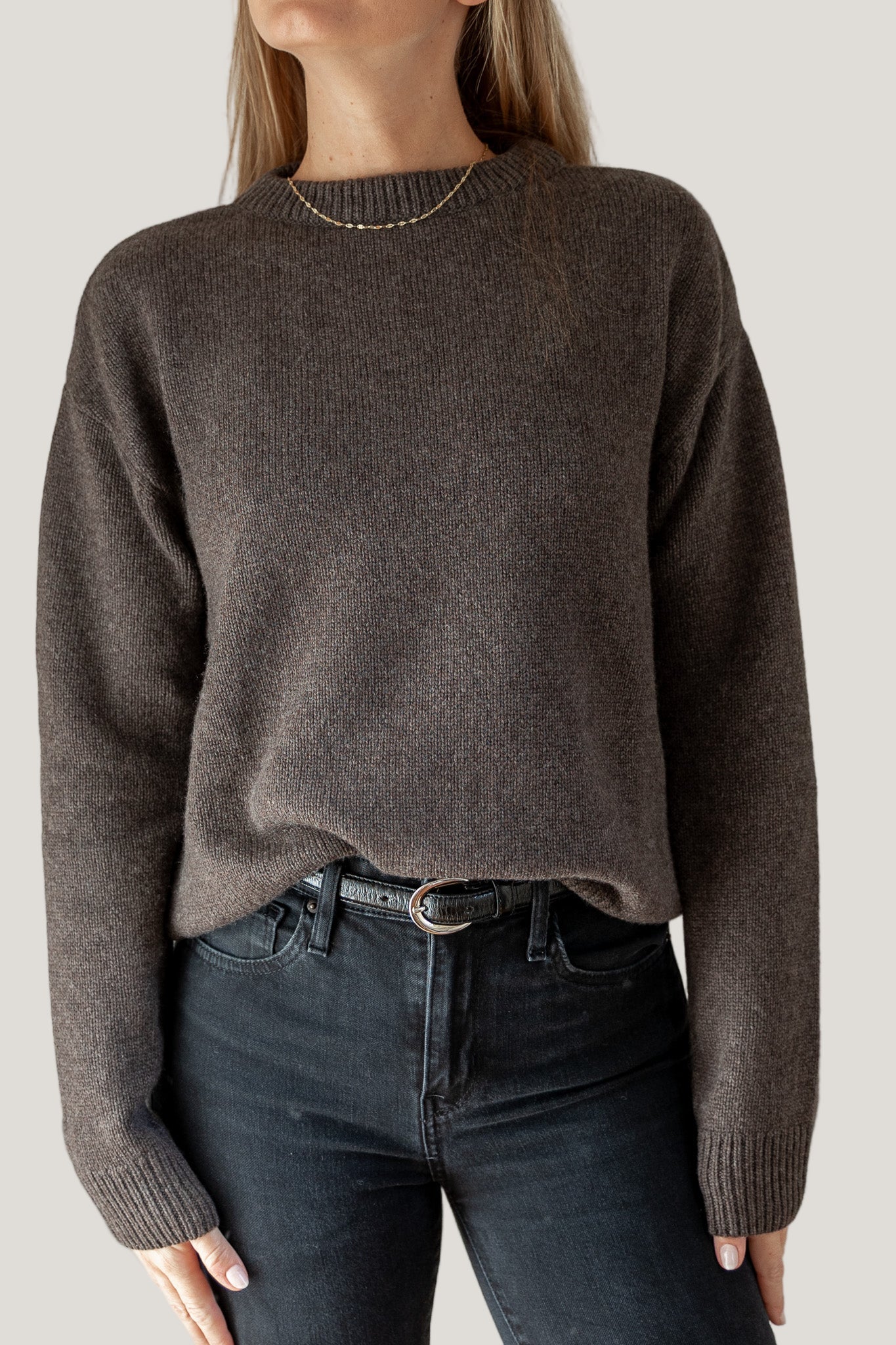 Person wearing a brown sweater and dark jeans on a plain background