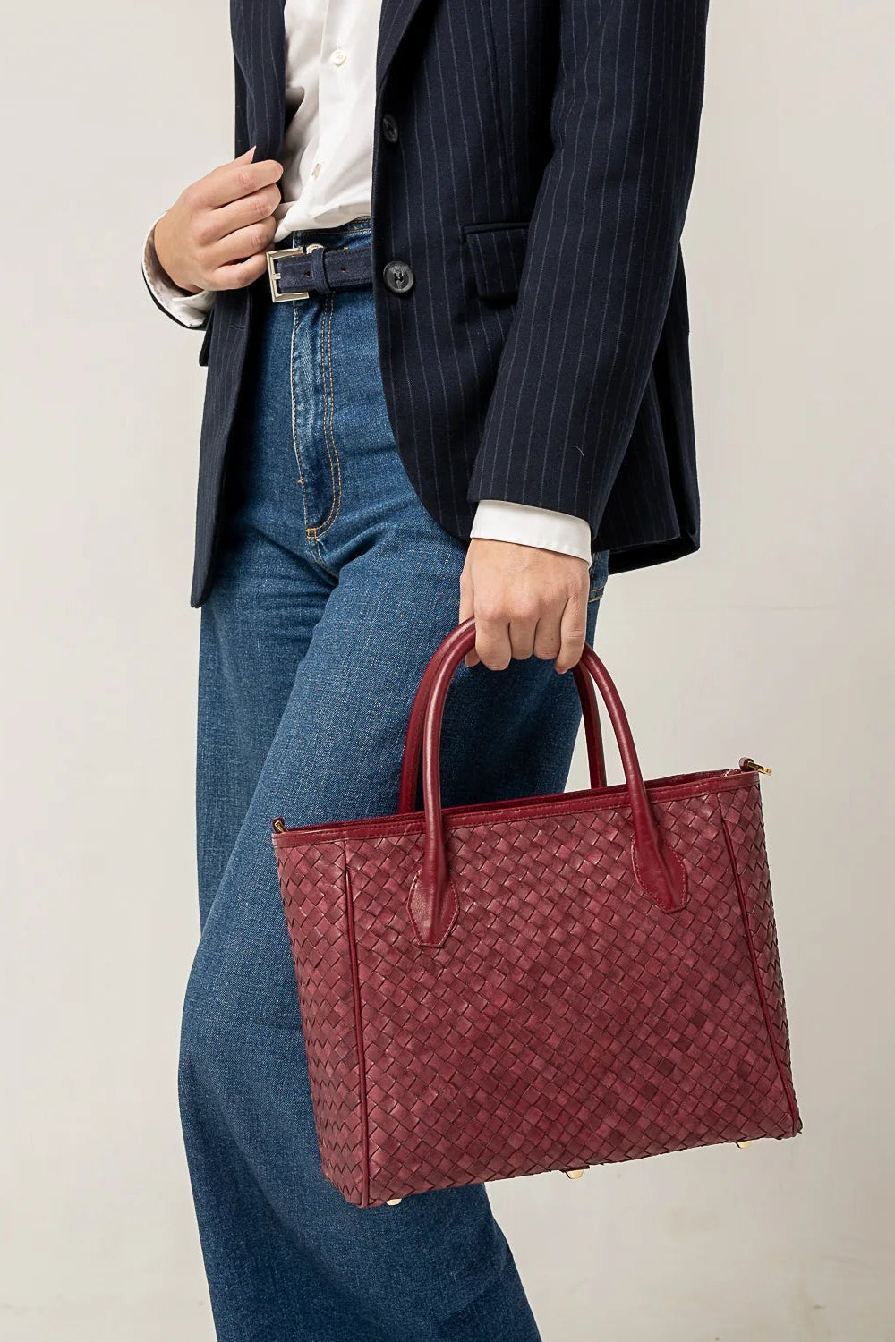 Person holding a red handbag wearing a dark suit and blue jeans against a plain background