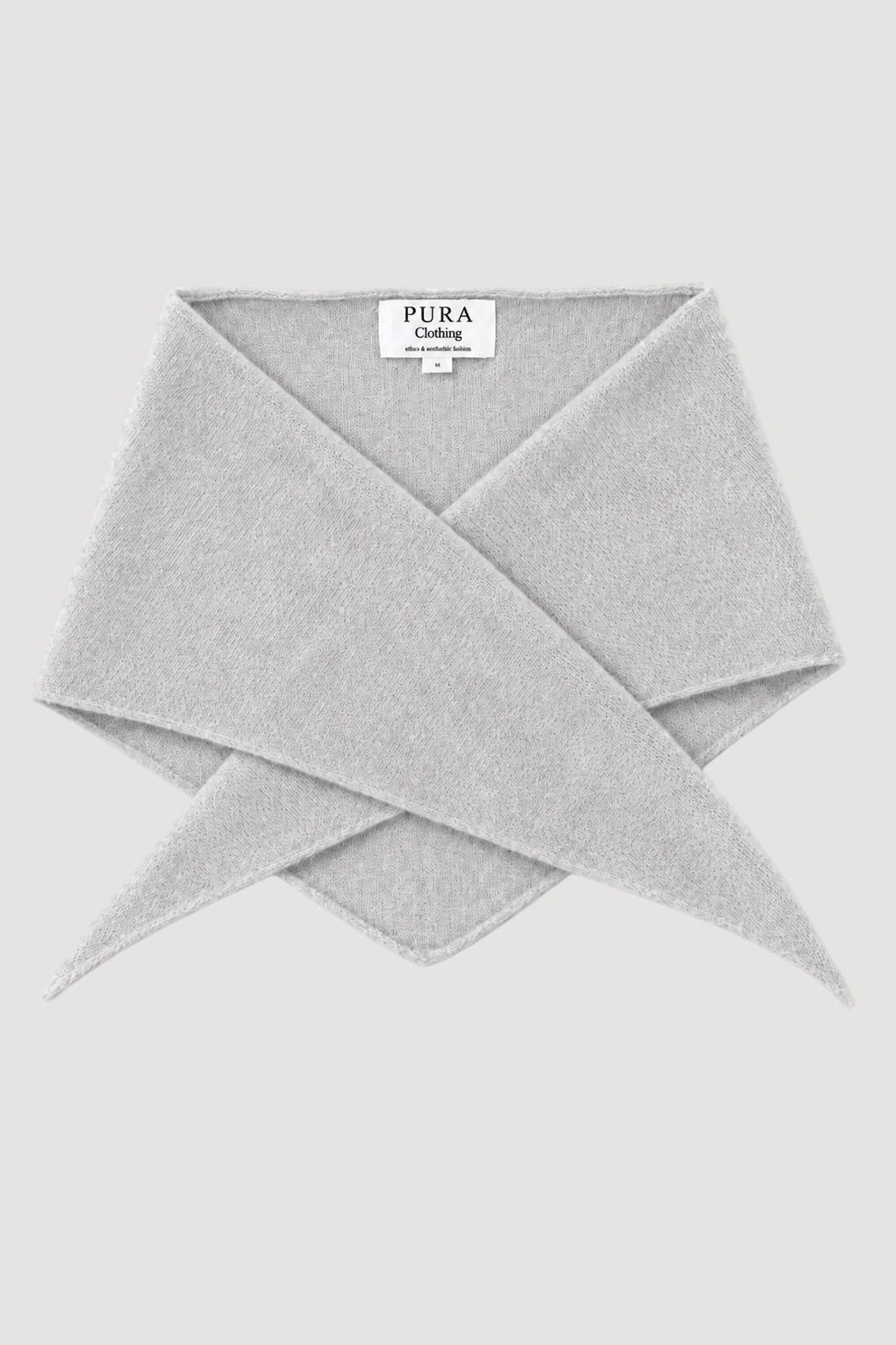 A light gray knit scarf folded in a cross-over style, with a white brand label reading 'PURA Celine' visible at the top center, on a solid light gray background.