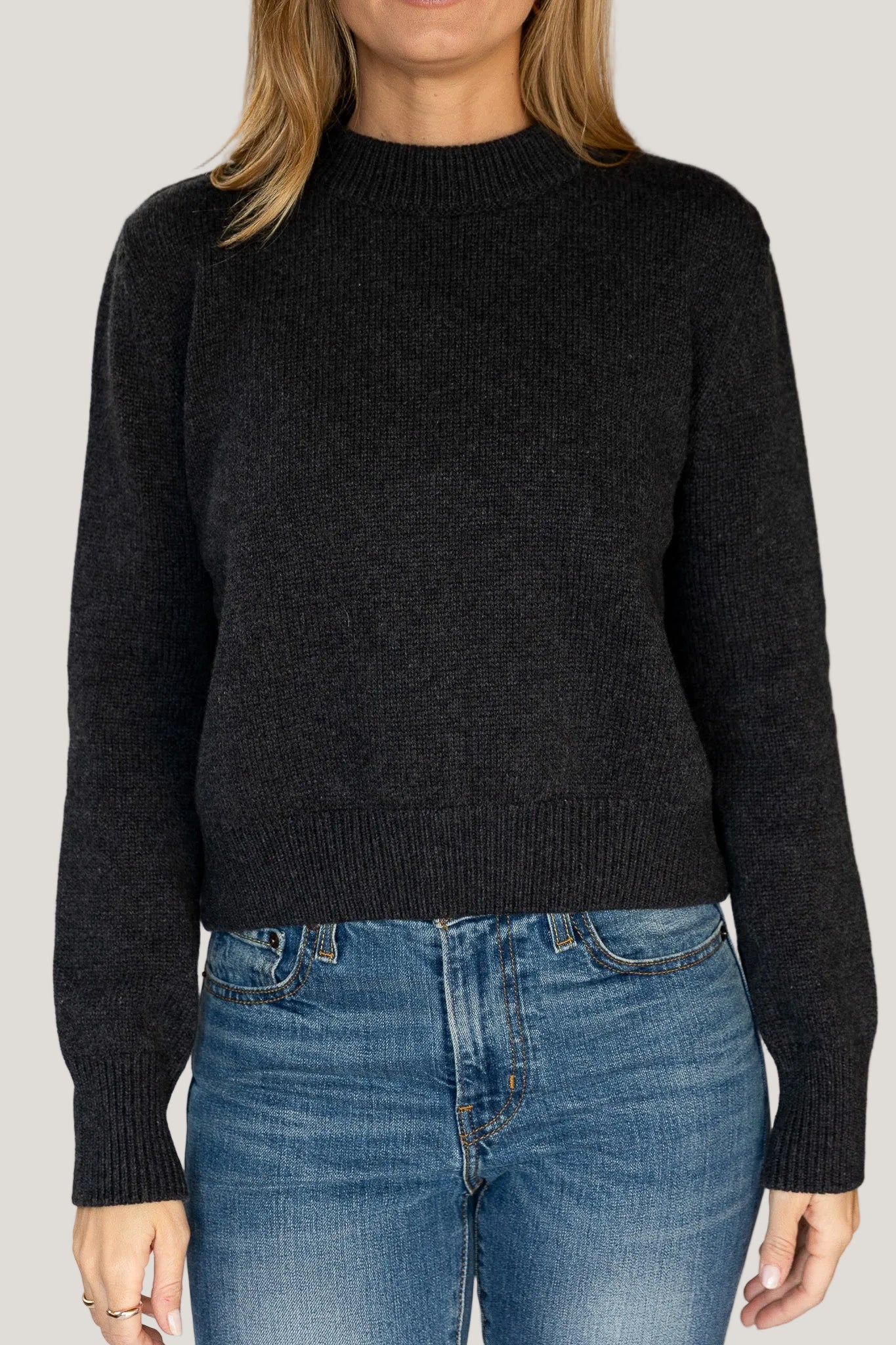 Person wearing a black sweater and blue jeans against a white background