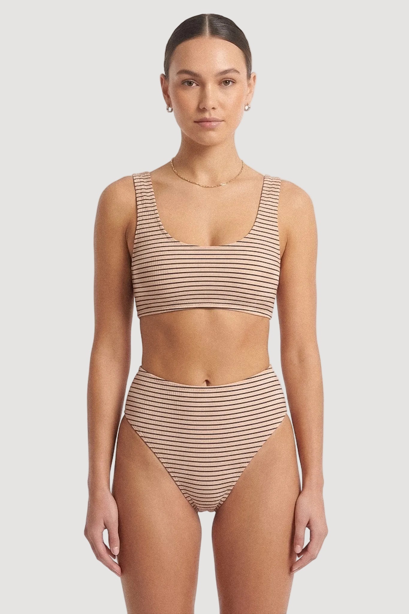A woman modeling a two-piece bikini set with thin beige horizontal stripes against a plain white studio background.