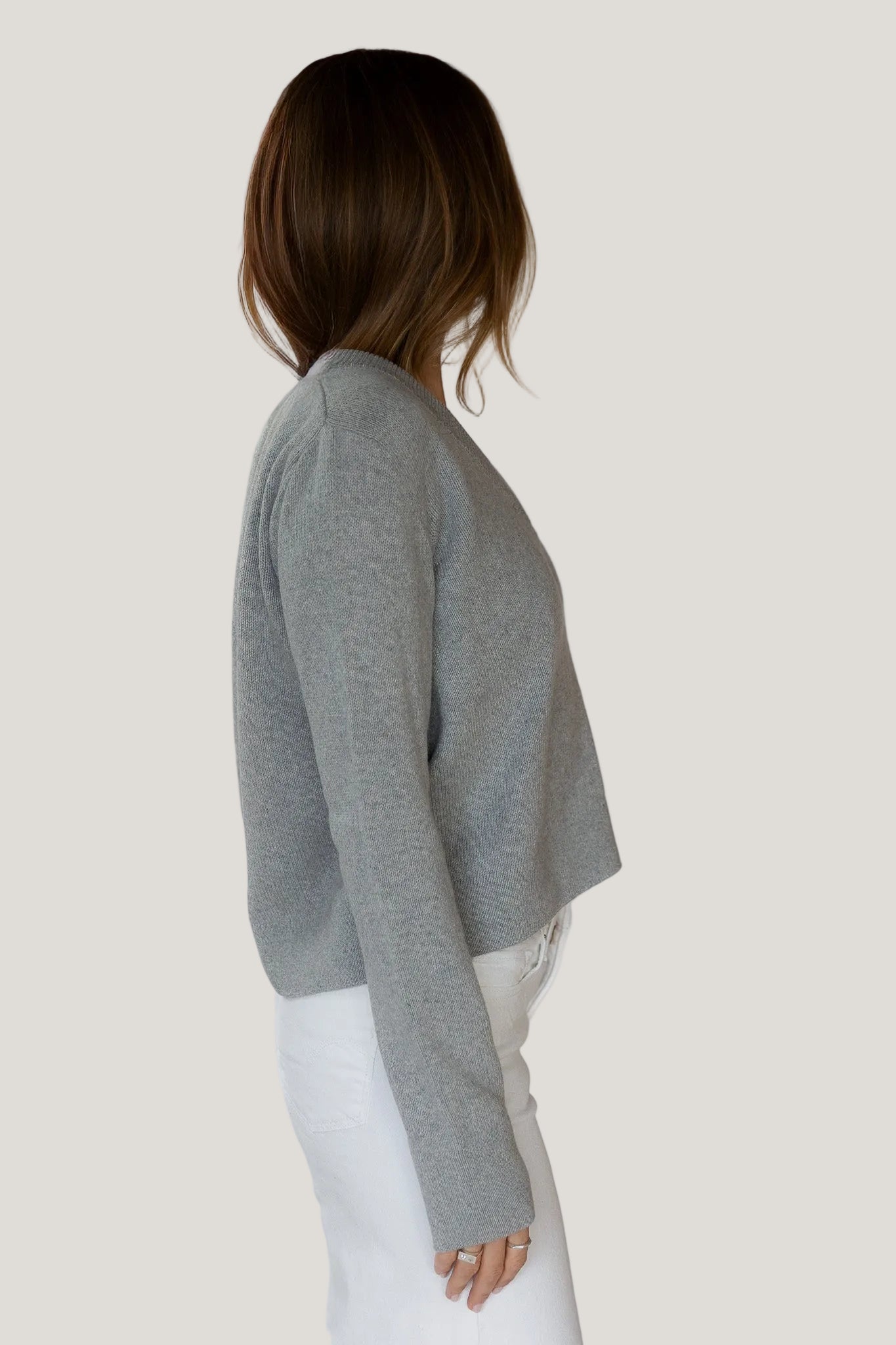 Person wearing a gray sweater and white pants against a white background