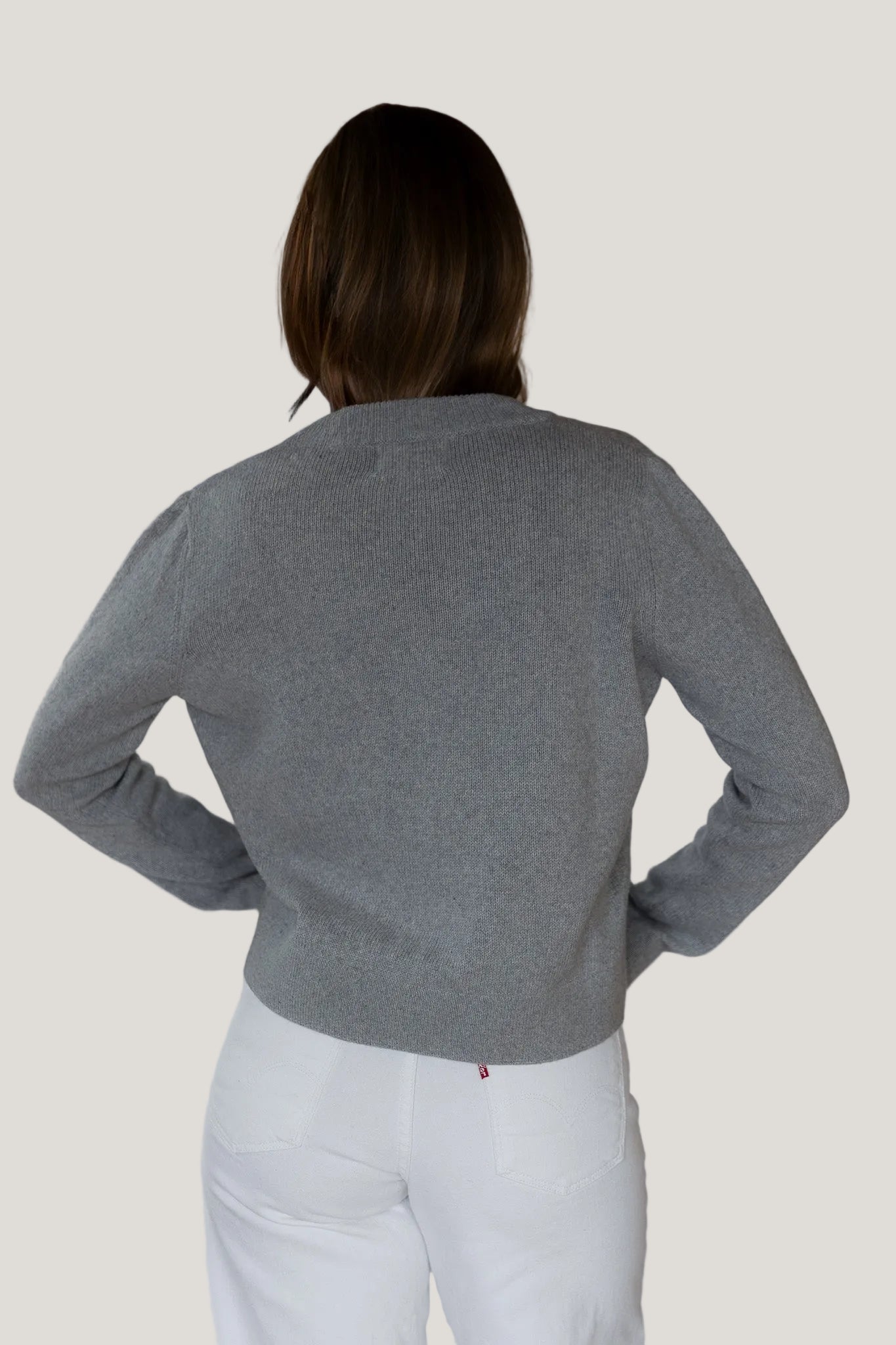 Person wearing a gray sweater and white pants against a plain background