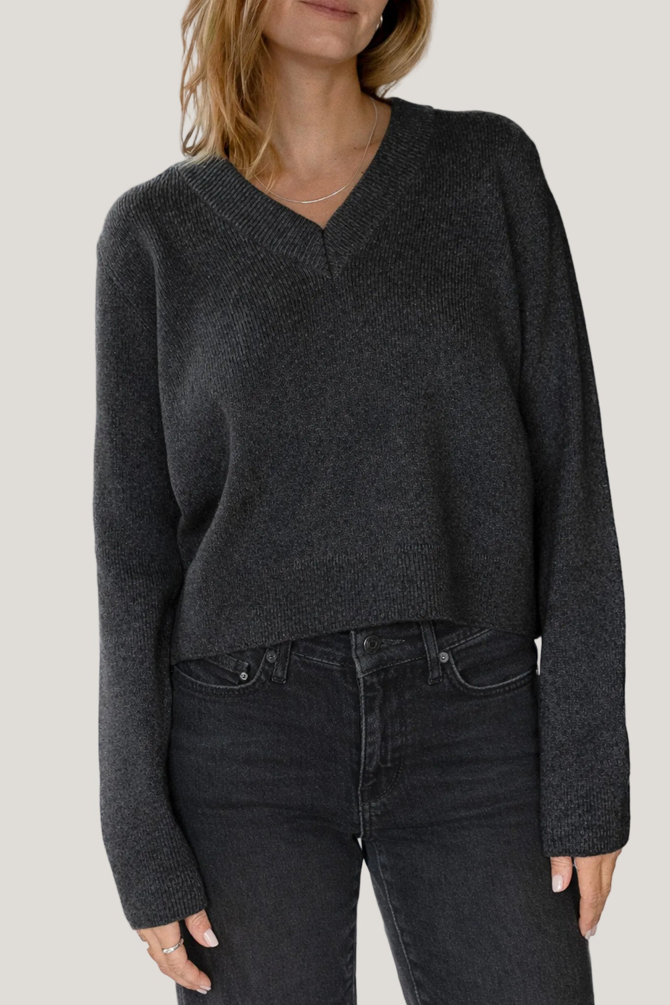 Person wearing a dark gray sweater and black jeans on a white background