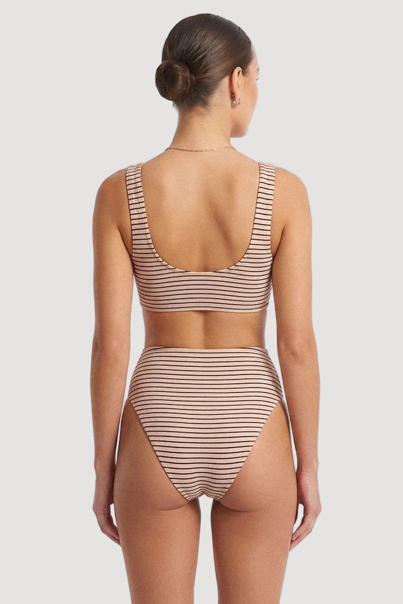 A woman shown from the back wearing a two-piece bikini with thin horizontal stripes in beige and brown, set against a plain white studio background.