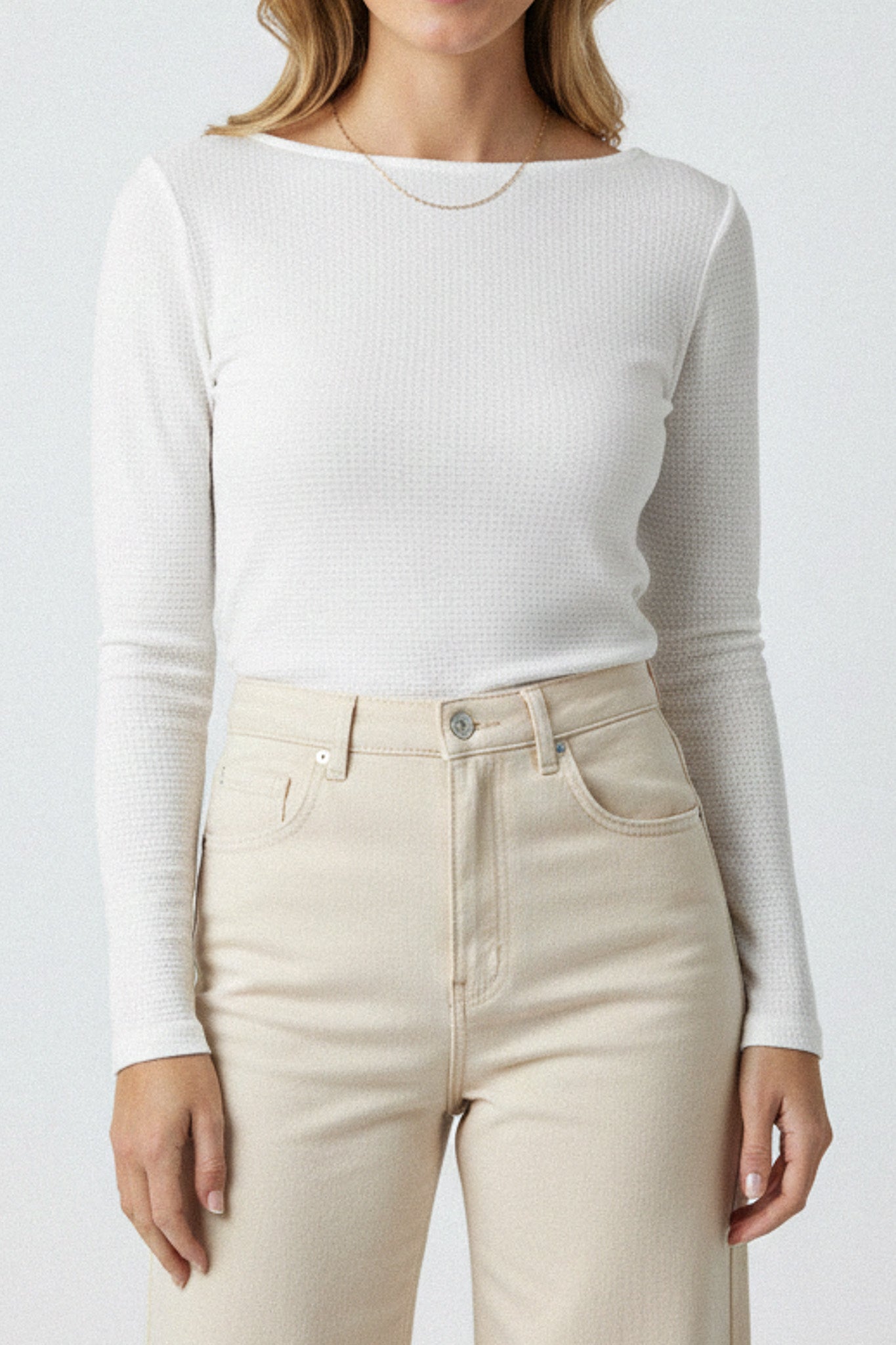 Person wearing a white ribbed long-sleeve top and beige jeans on a plain background