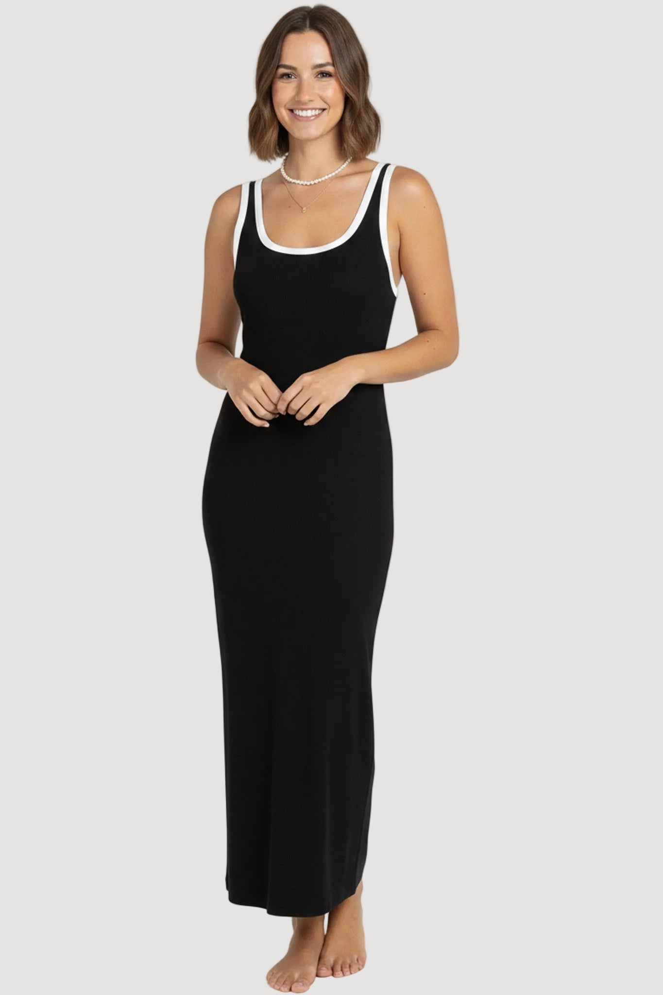 Woman wearing a black sleeveless dress with white trim on a white background