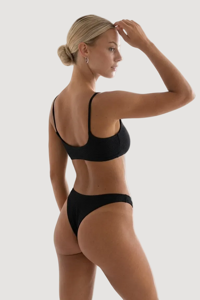 Woman wearing a black bikini in a minimal indoor setting