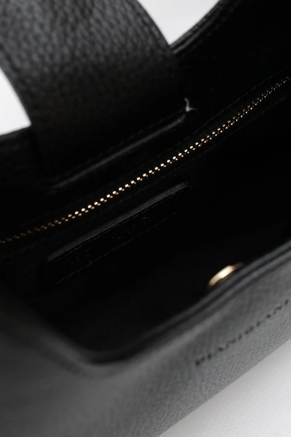 Close-up of a black handbag with gold hardware on a light gray background