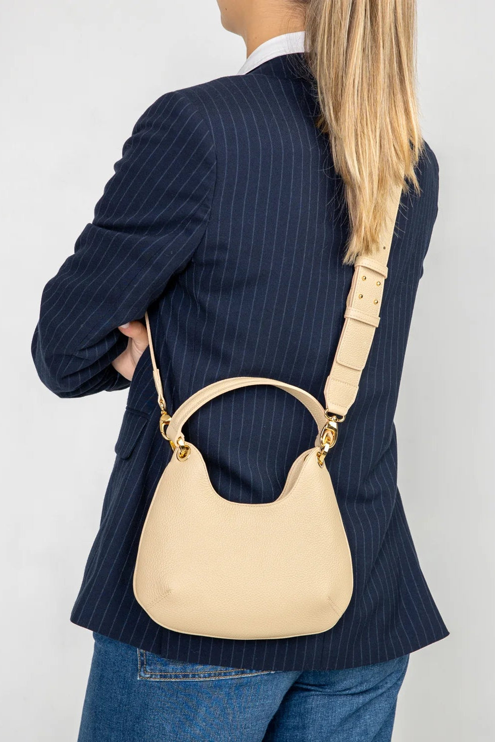 Person wearing a navy pinstripe blazer with a beige handbag on a plain background