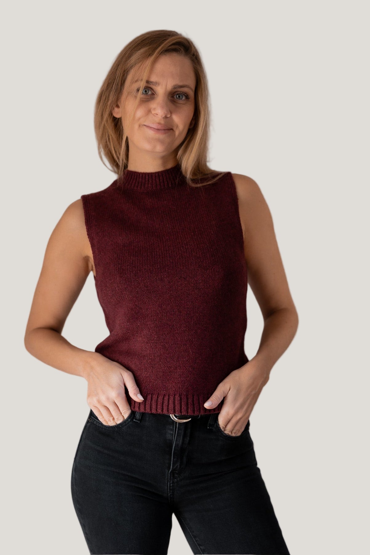 Woman wearing a burgundy sleeveless sweater against a plain background