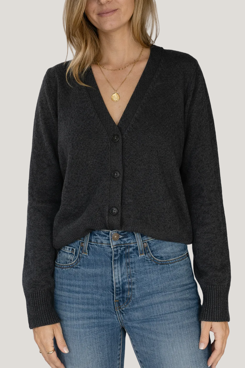 Person wearing a dark gray cardigan and blue jeans against a white background