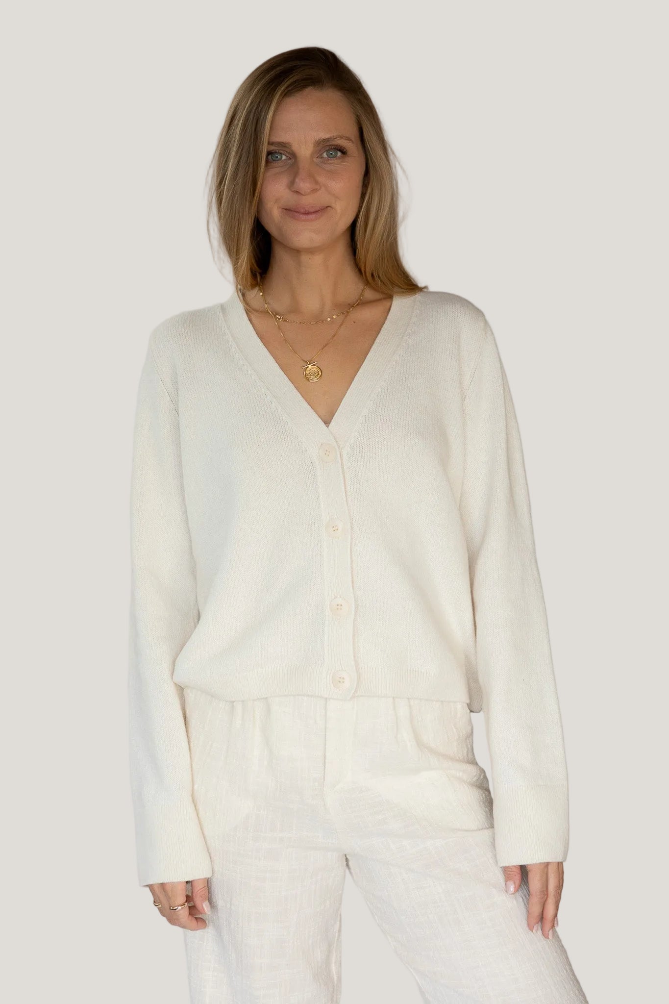 Woman wearing a cream-colored cardigan against a plain background