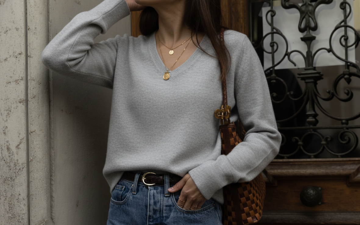 Person wearing a light gray sweater and blue jeans, standing against a textured wall.